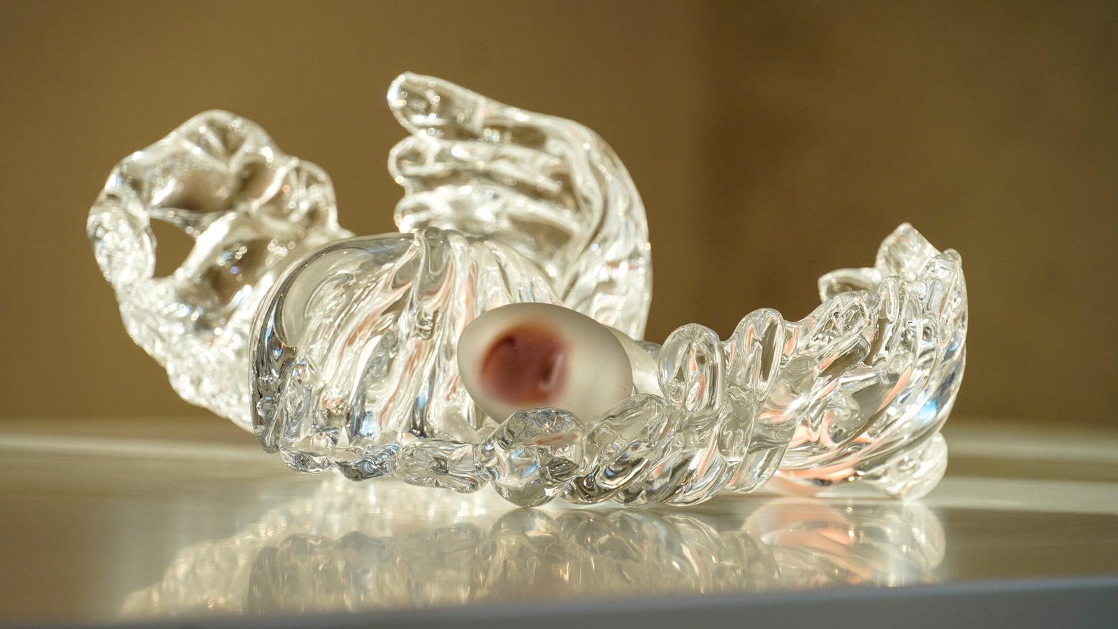 A ribbed clear glass vessel lit from the side, a pale nodule resting inside