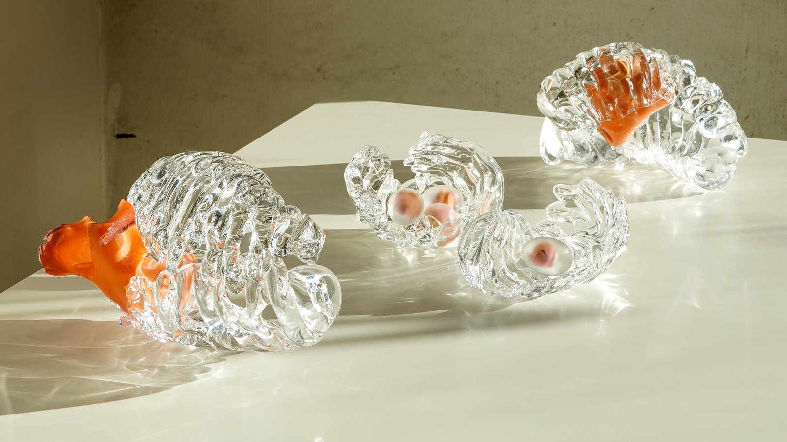 Three glass forms arranged across a lit white plinth