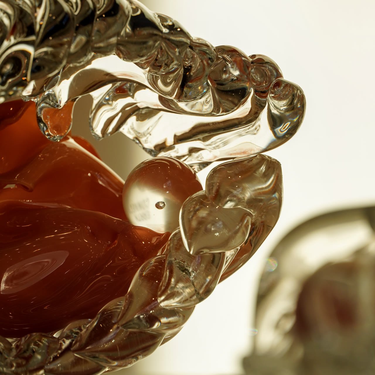Detail of a deep red hollow cradling a pearl-like sphere inside ribbed glass