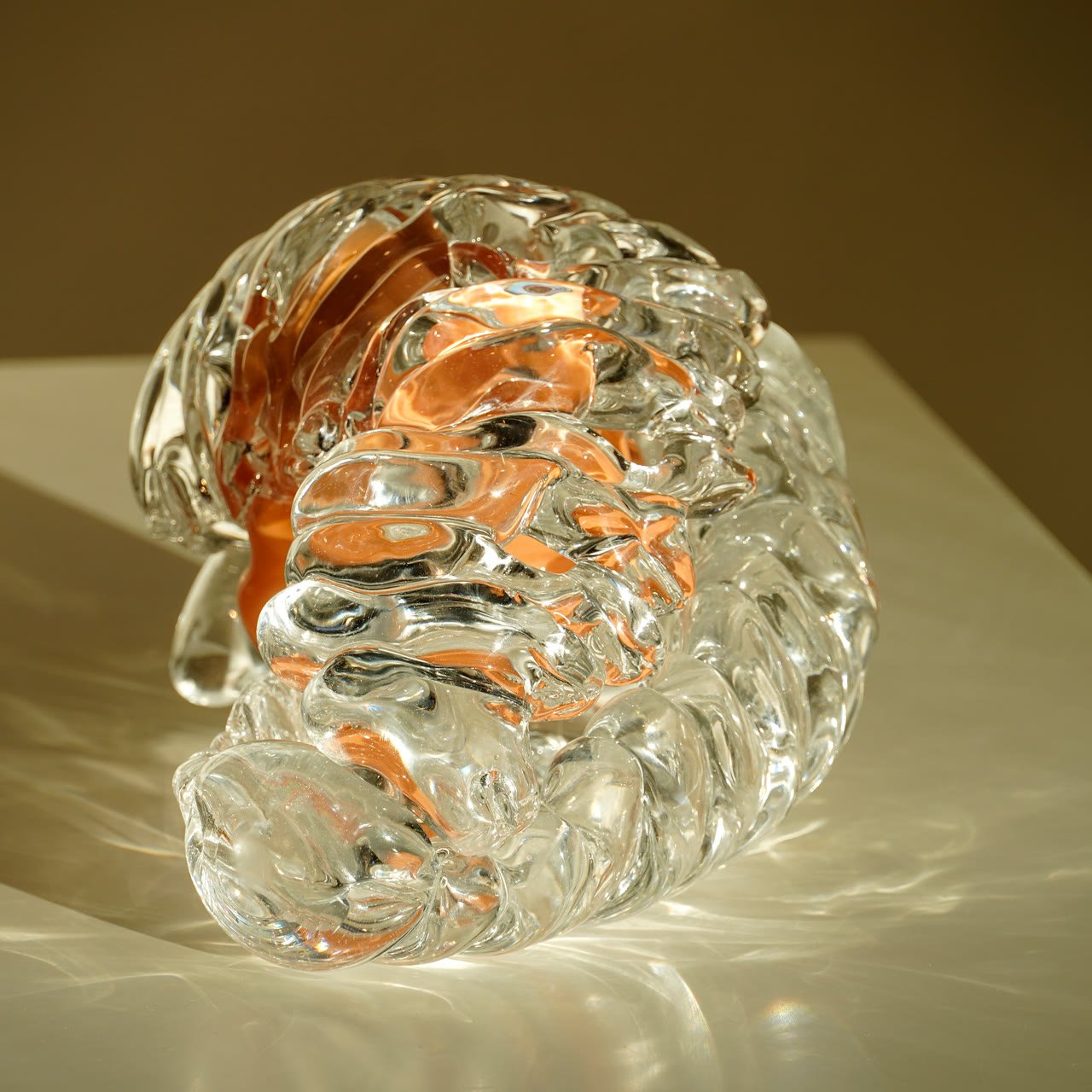 A curled ribbed glass form with an amber core on a white plinth