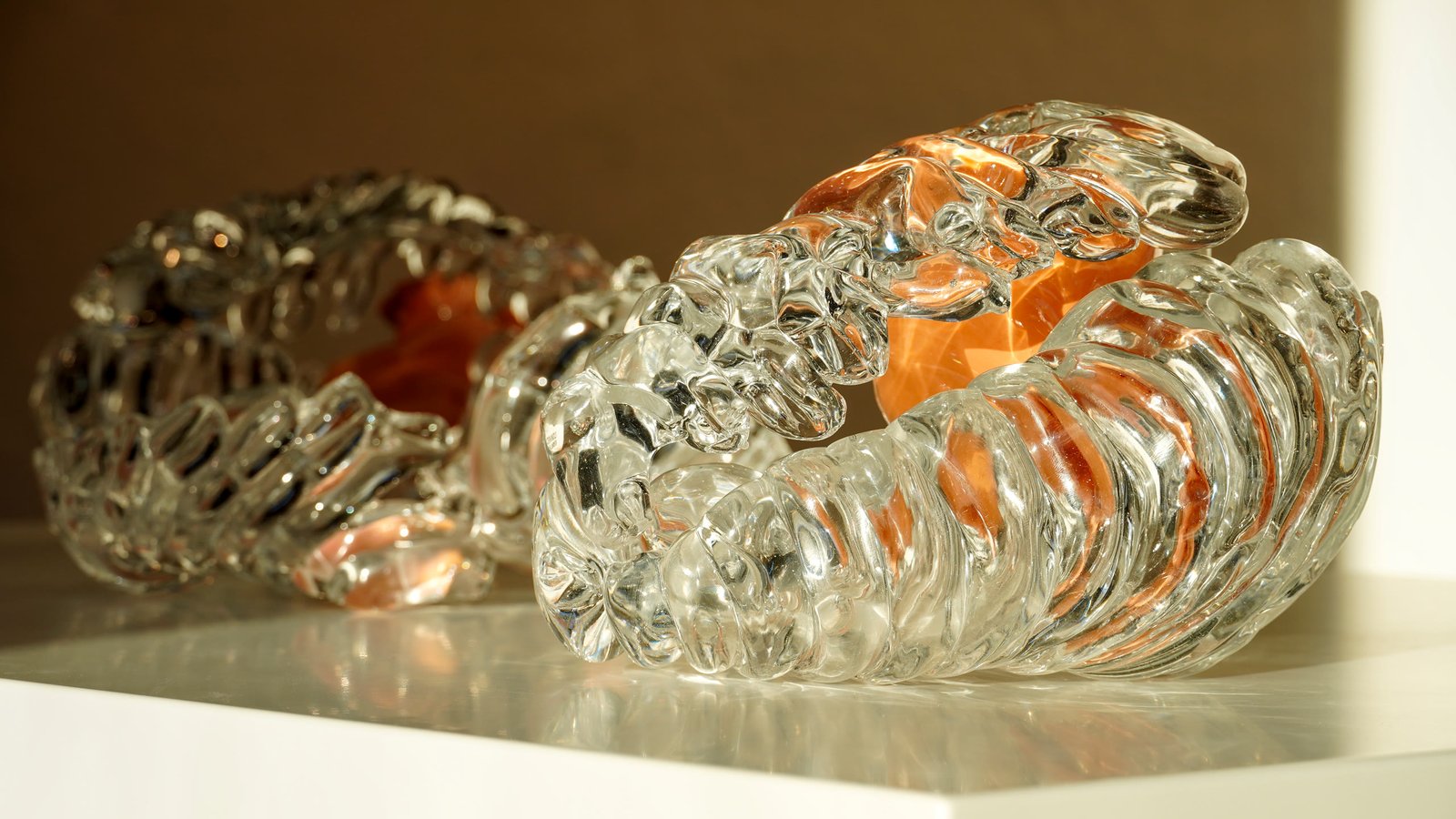 Two glass pieces on a white plinth, one opening onto an orange interior