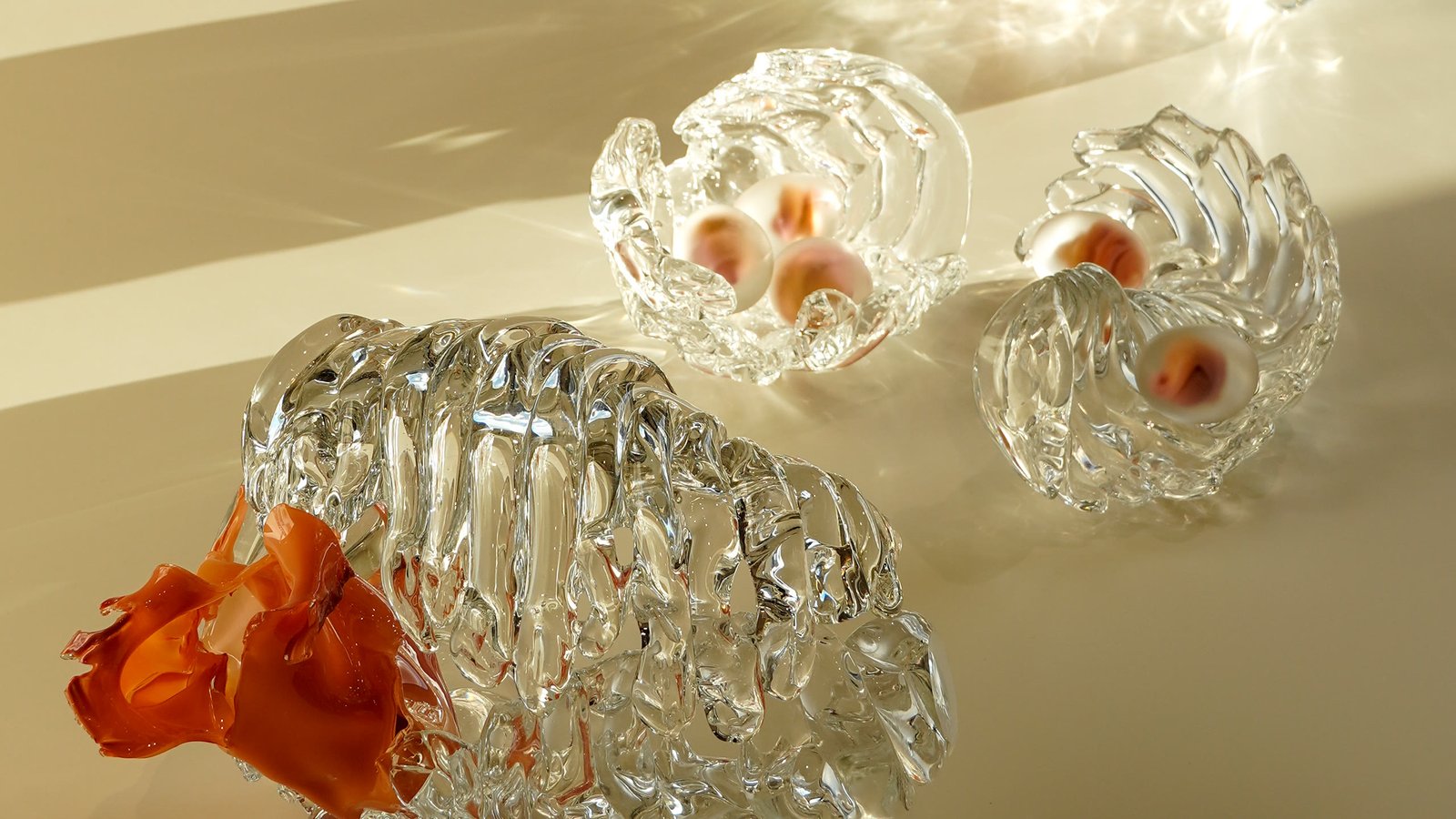 Three pieces on a lit surface, the nearest opening onto orange glass