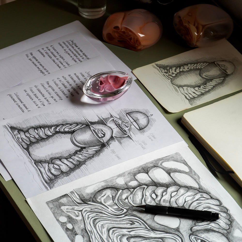 An open sketchbook of drawings beside a glass piece and written notes