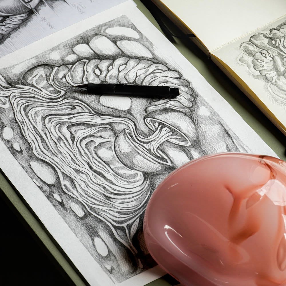 A detailed graphite drawing with a pen resting on it, a glass piece in front