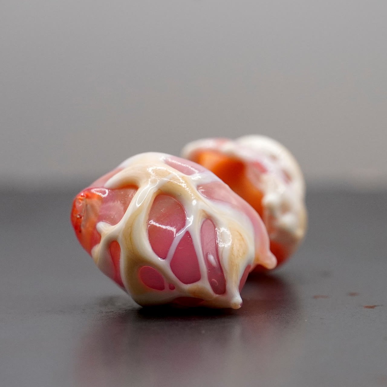 Two cream and pink webbed flamework forms on a dark surface
