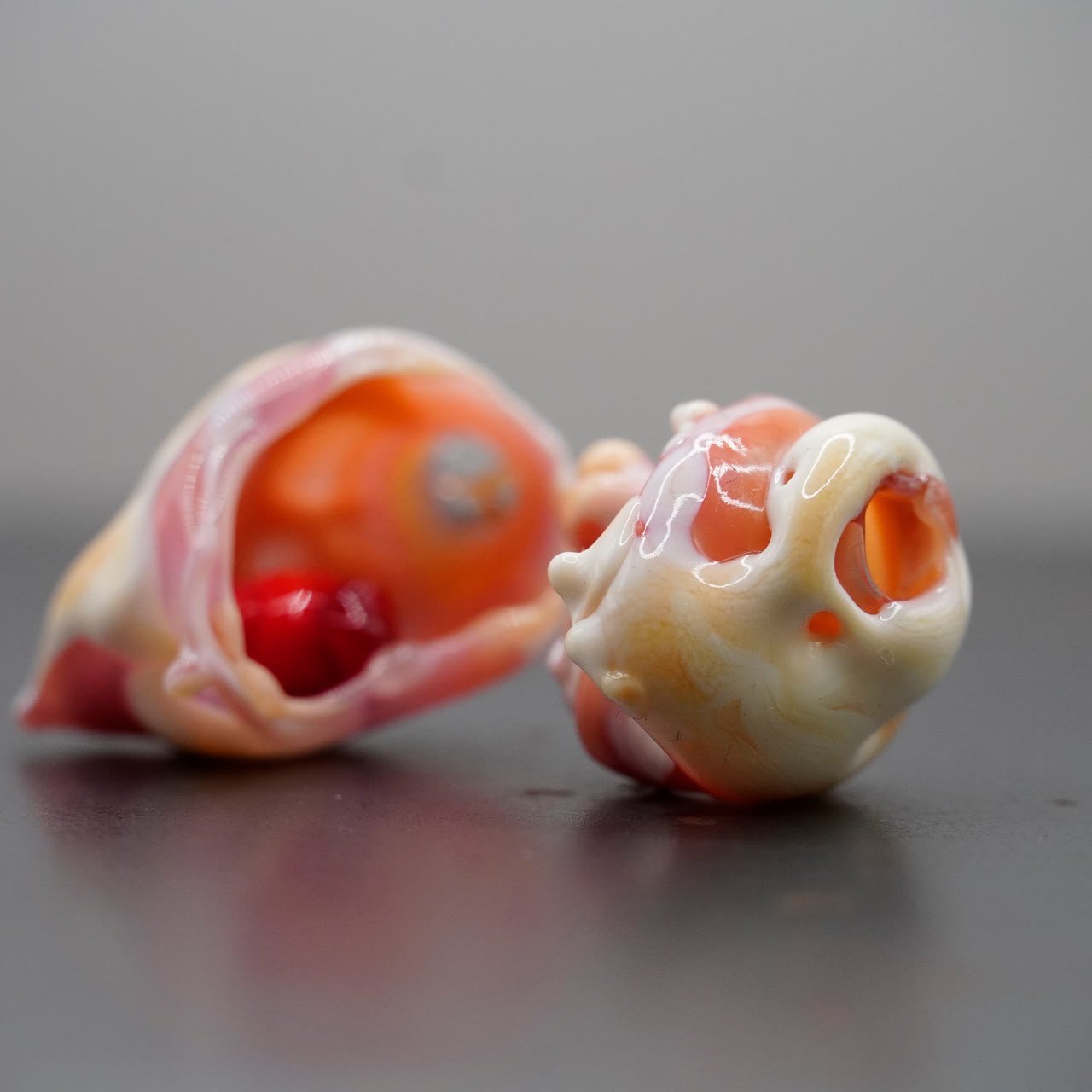 Two flamework pieces on dark steel, one open onto an orange interior