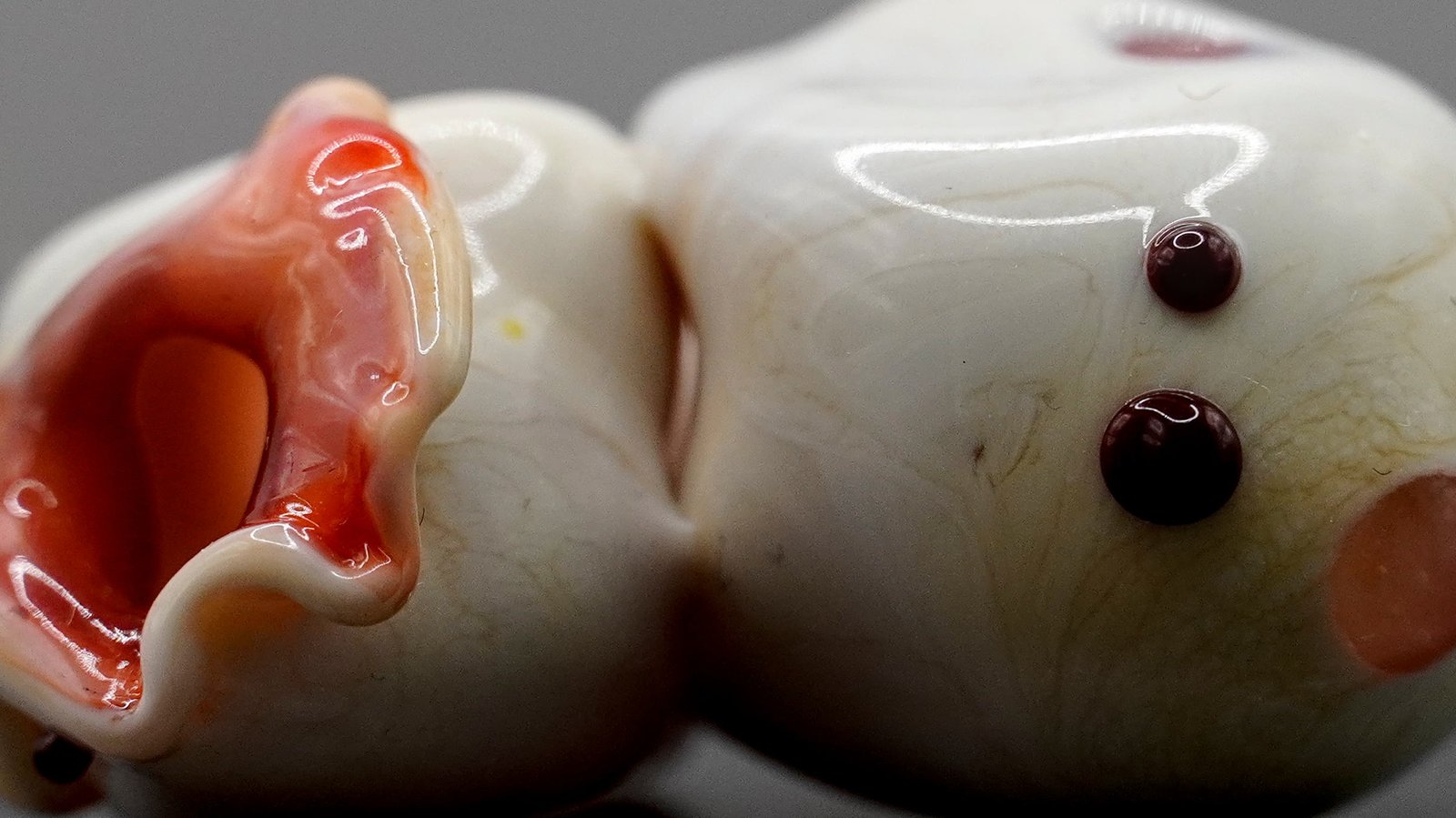 Close detail of two bone-white glass lobes with dark beads and a pink opening