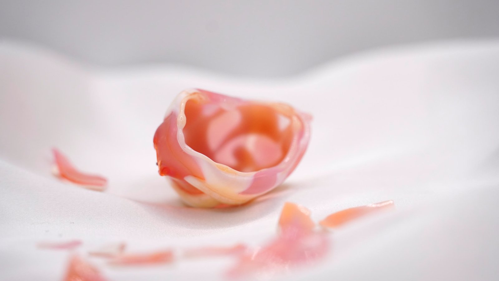 A small open cup form in flesh pink on white cloth