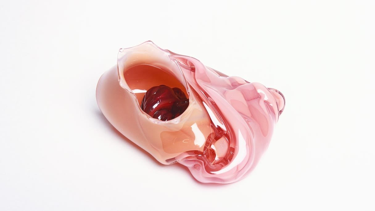 A pale pink glass form opening onto a deep red core, on white