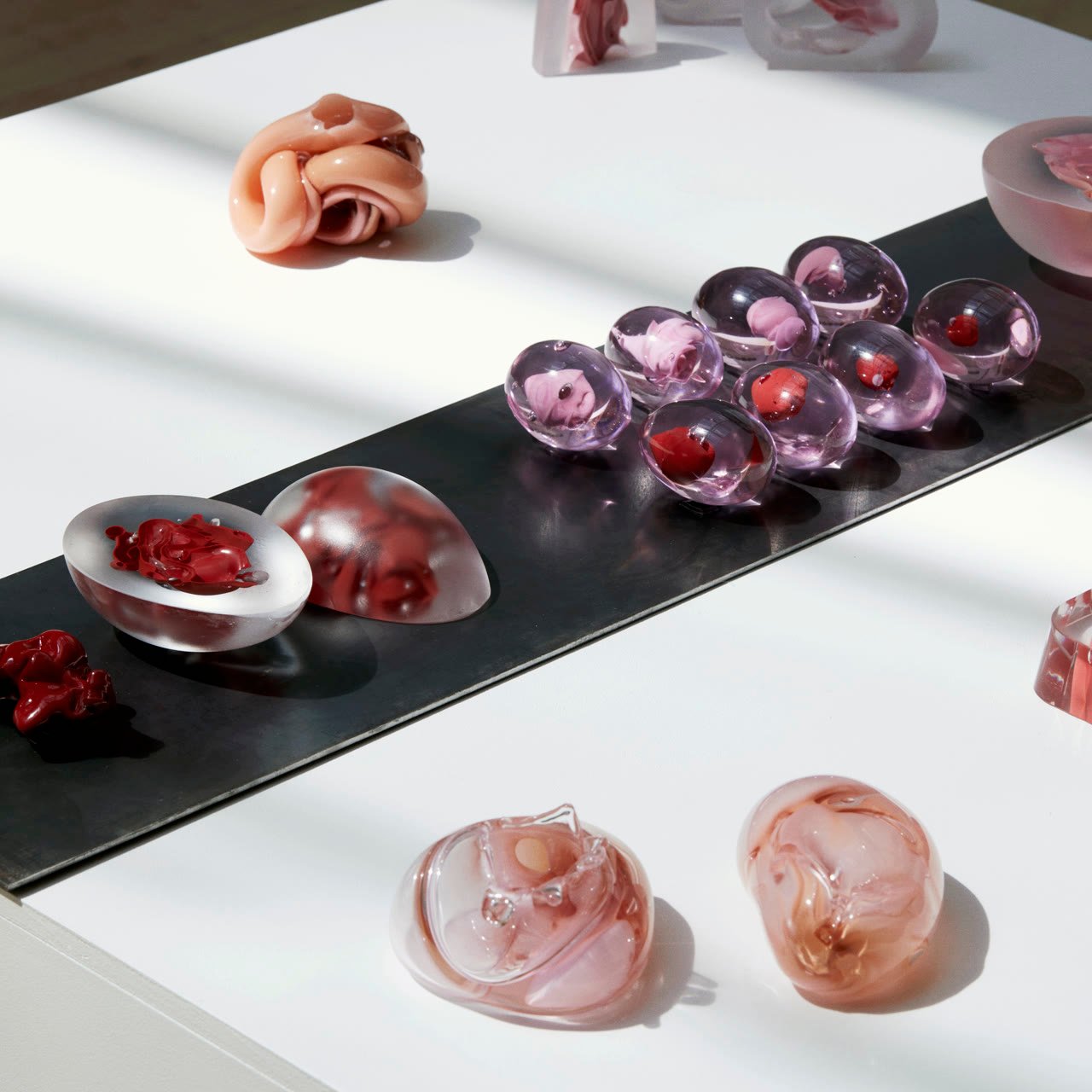 Glass pieces laid out across a white table and steel bench in the studio