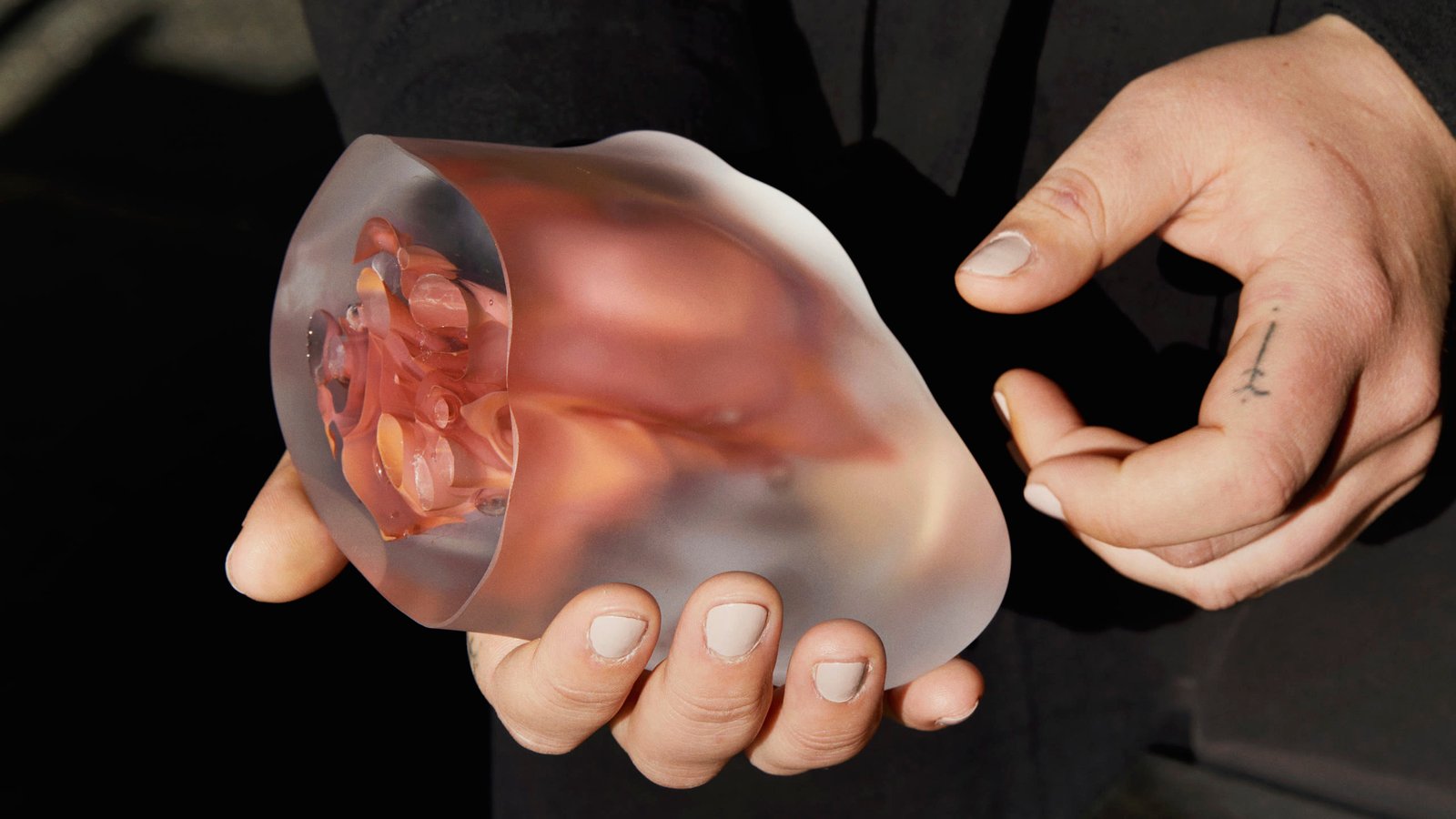 Hands cradling a frosted glass vessel with a pink interior