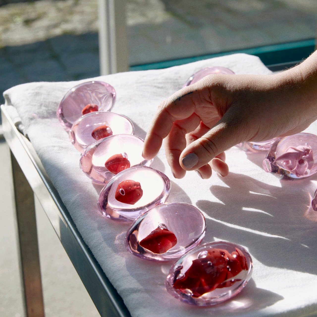 A row of pink glass domes with red cores on white cloth, a hand reaching in