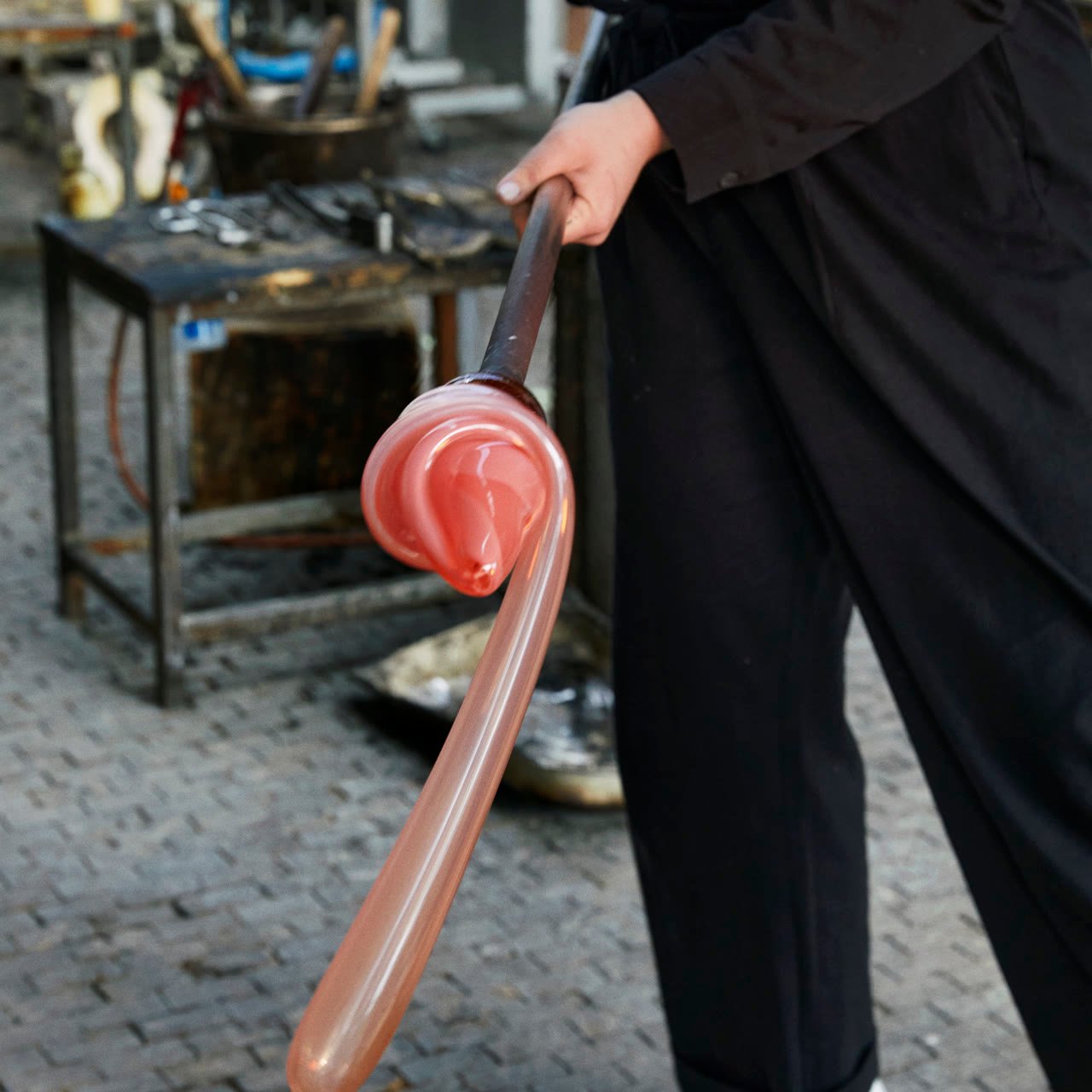 A blowpipe with molten pink glass gathered at its end, in the studio
