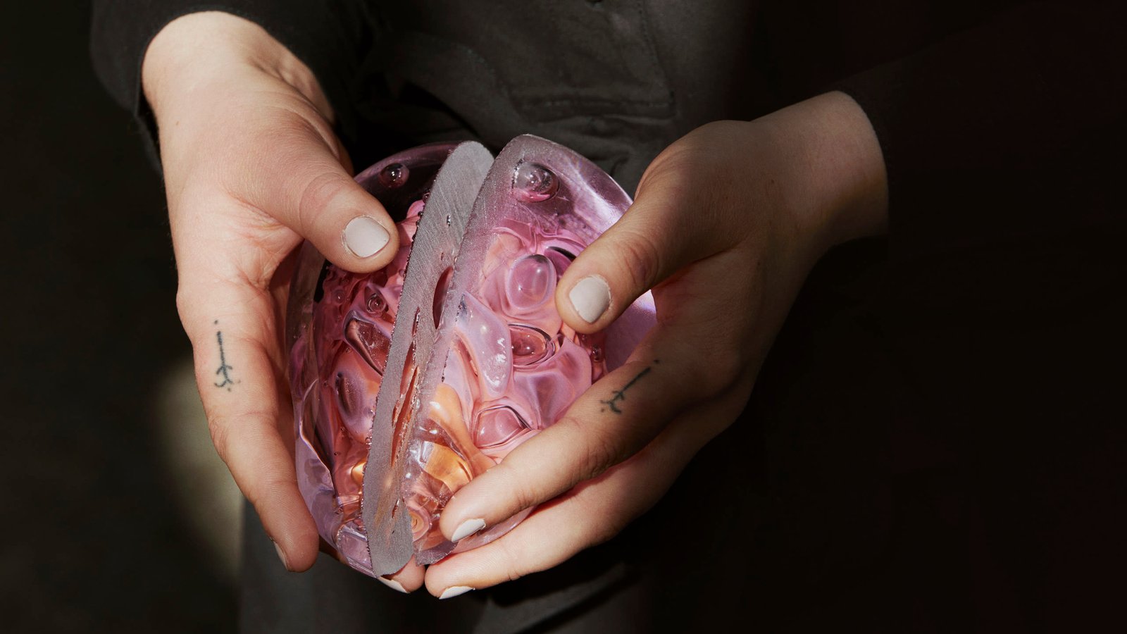 Hands holding a pink and amber glass form against a dark ground