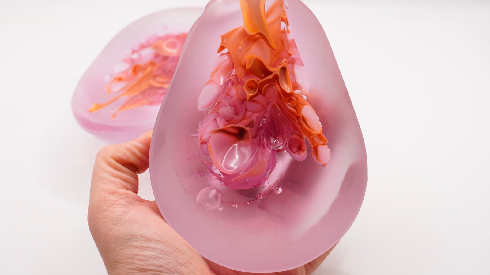 A hand holding a frosted mauve dome with an amber form inside