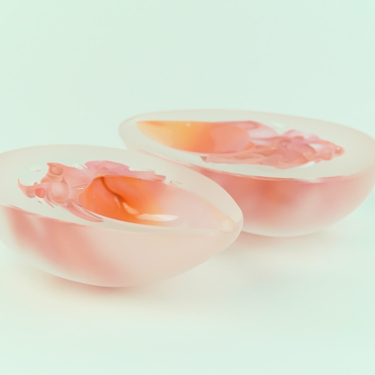 Two frosted bowls side by side, coral interiors, on pale mint