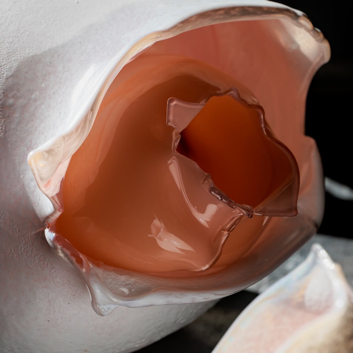Close-up of the opening: layers of smooth coral glass folding inward inside the white frosted shell.