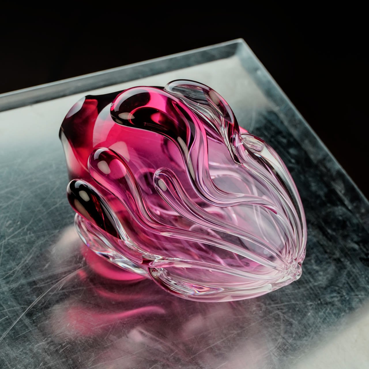 A magenta-cored pink glass form on a scratched steel plinth
