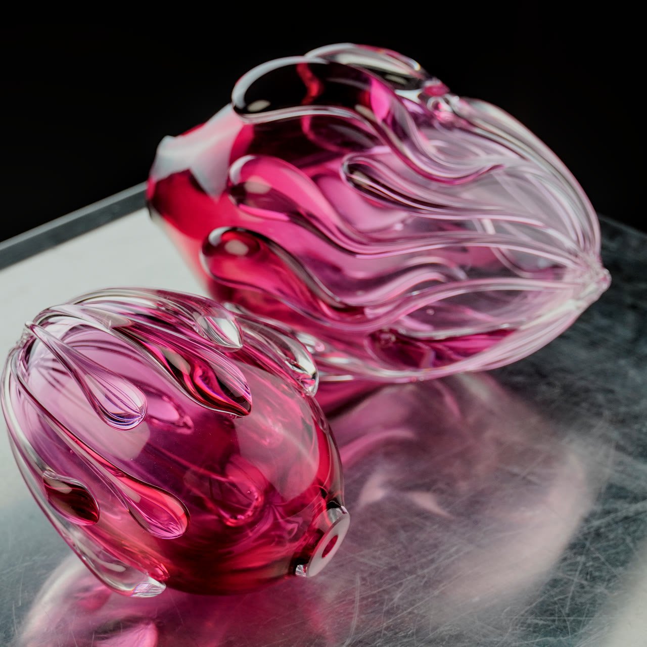 Two pink glass forms resting on a steel surface