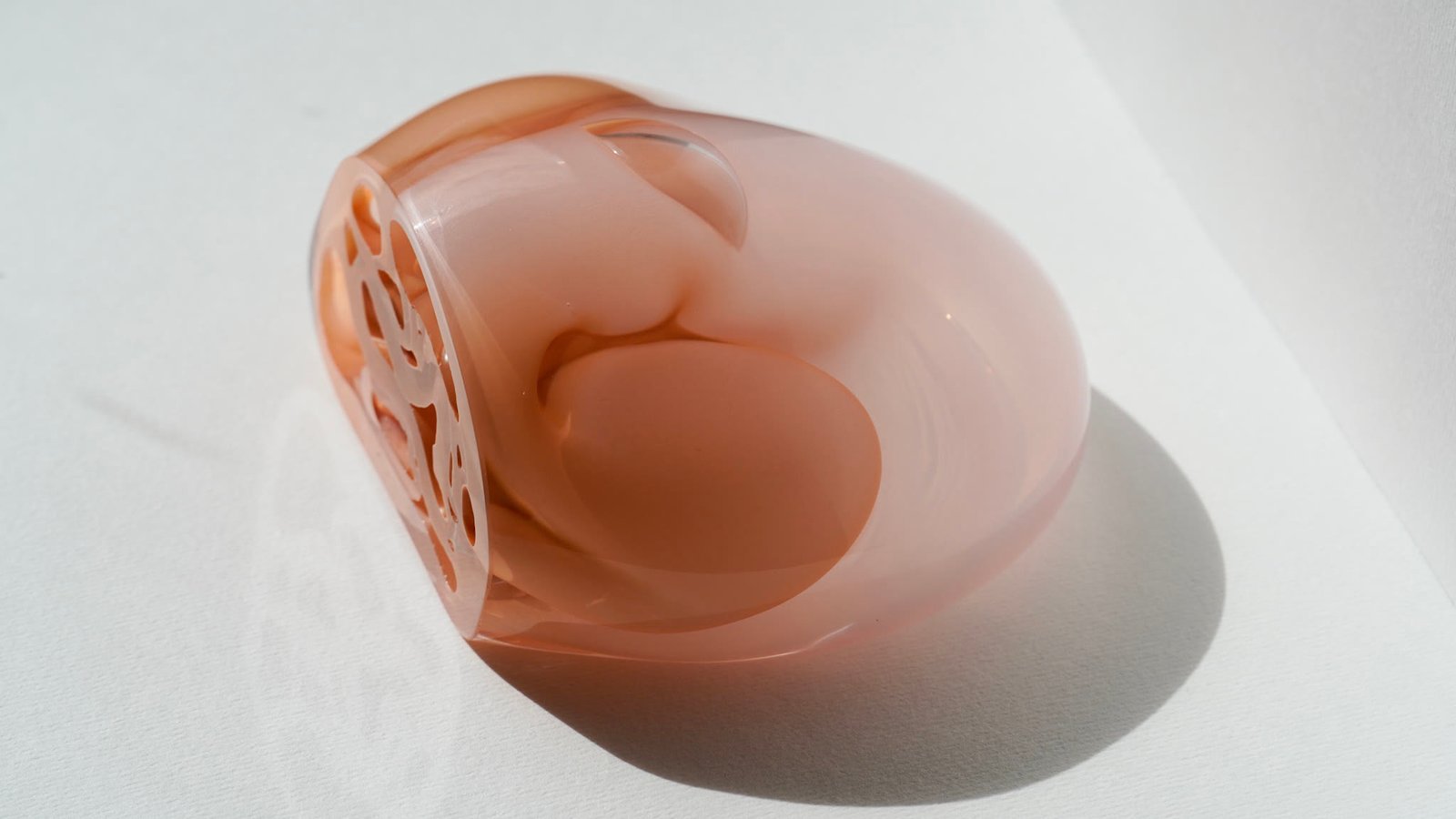The blush glass form casting a long shadow on white
