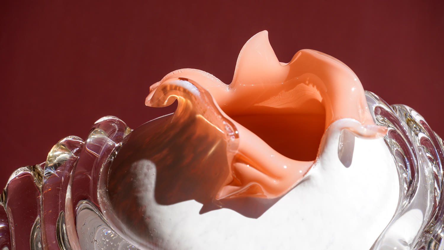 A vase with a coral ruffled rim and white body against deep red