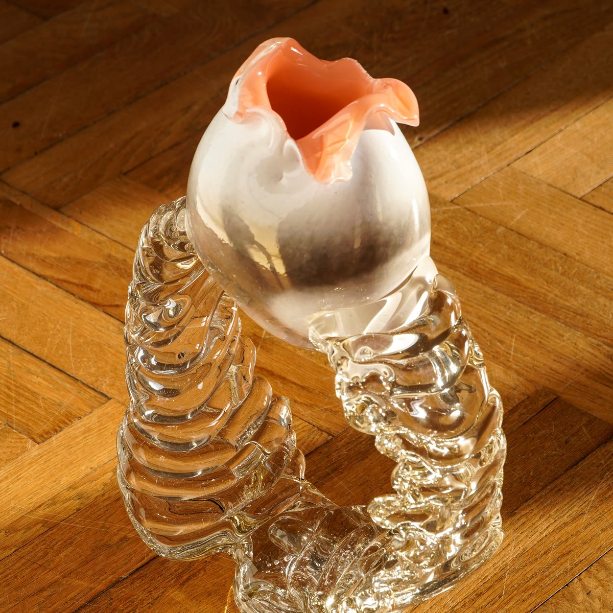 A vase on a parquet floor, its clear ribbed base twisting beneath
