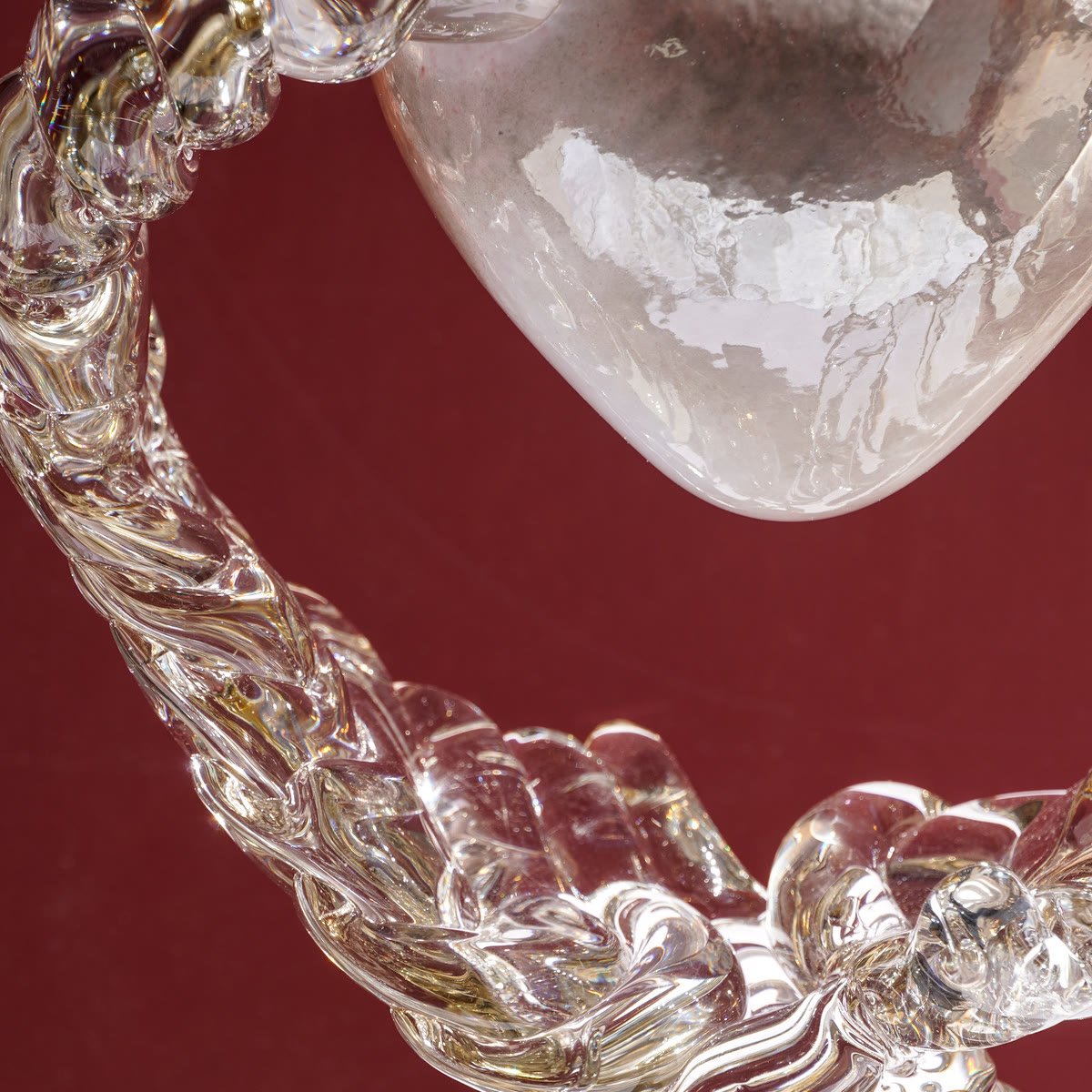 Close detail of the twisted clear glass loop against deep red