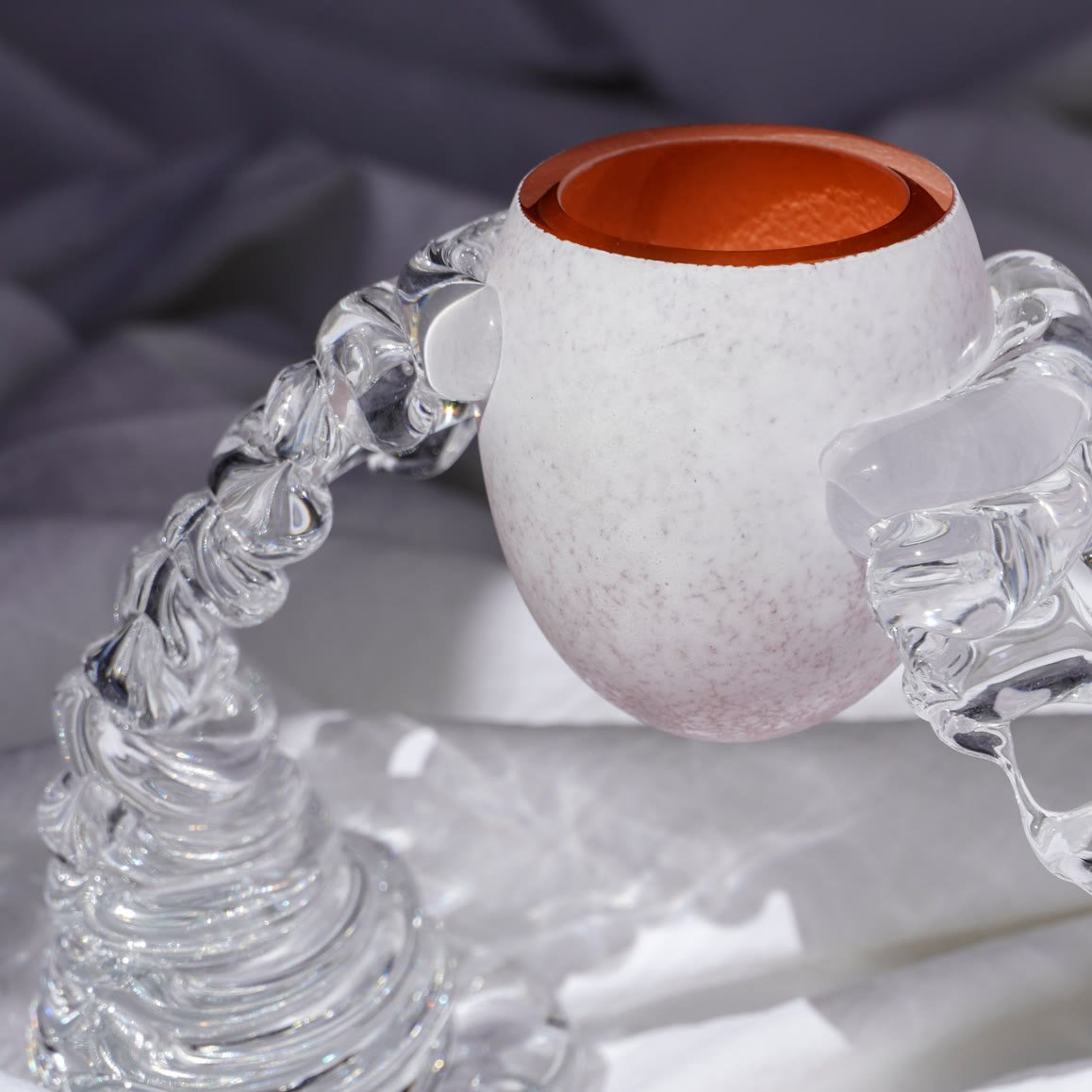 A speckled white vase with a terracotta mouth and a looping ribbed base